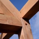 Douglas fir beams joined in an outdoor timber frame structure under a blue sky.