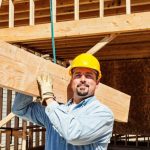 Worker carrying structural beams at a residential construction site.