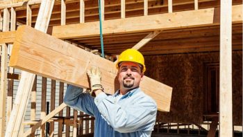 Worker carrying structural beams at a residential construction site.